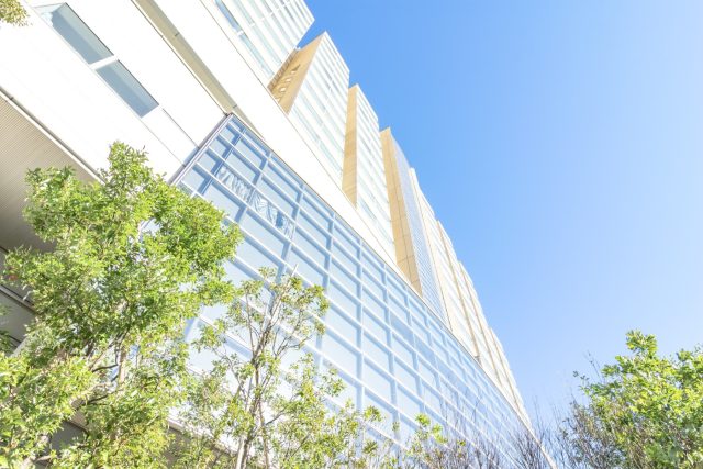 介護施設の建物外観。青空の下、モダンな多層階の白を基調とした建築で、周囲に緑が配置されている。
