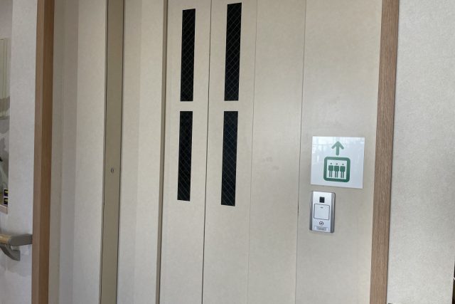 施設内のエレベーター扉。上向き矢印の案内表示と呼び出しボタンが見える。